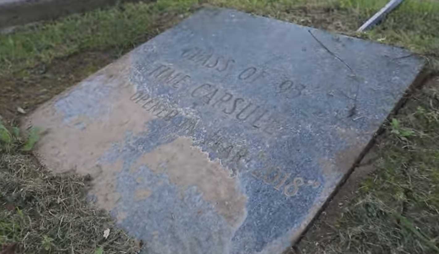  A stone slab on the ground with the words 'Class of 93 Time Capsule, Opened April 18, 2018' carved into it.